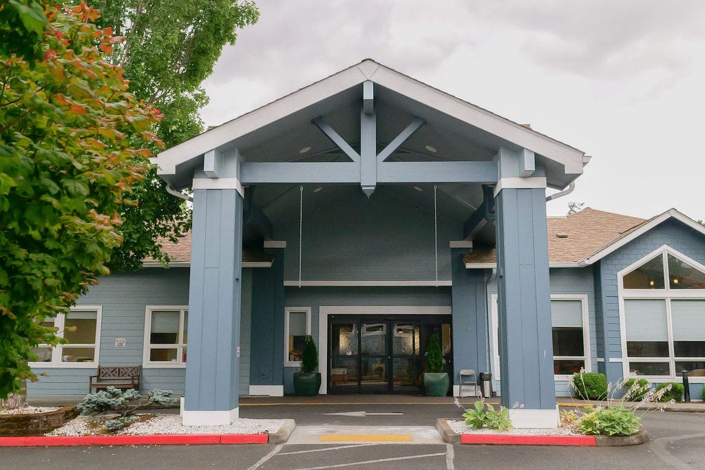 Main entrance of McLoughlin Place seen head on, with a blue porte-cochere over the drive and glass double doors